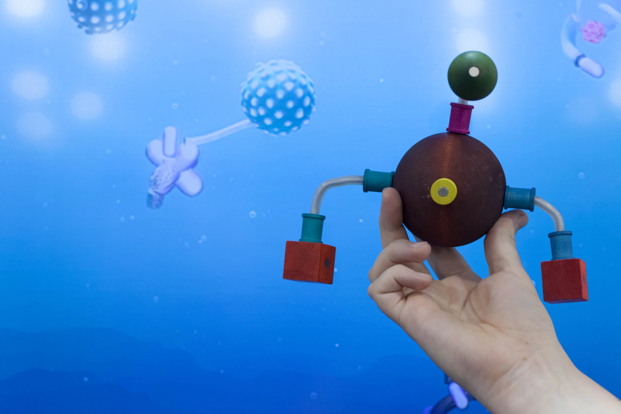 A hand holds a colorful modular creature in front of its blue digital-aquarium counterpart.